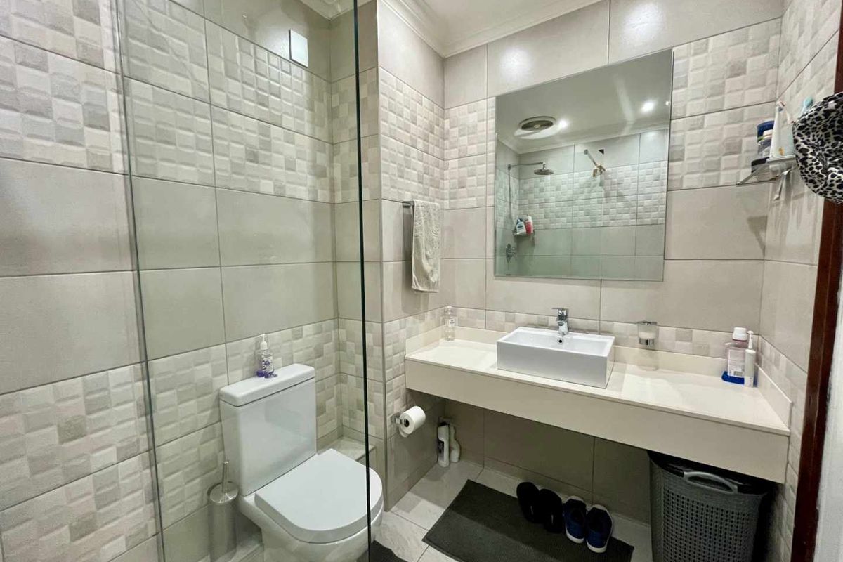 Modern bathroom featuring a glass-enclosed shower, wall-mounted vanity with a vessel sink, large mirror, and neutral tiled walls.
