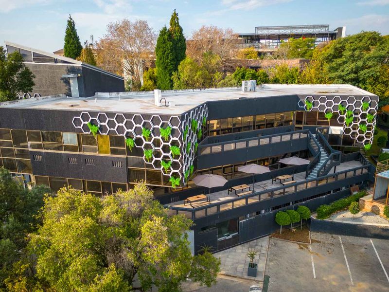 Aerial view of a modern office building featuring a unique honeycomb facade design, external terrace, and dedicated parking area.