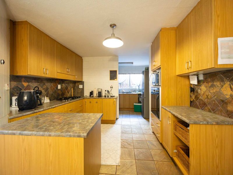 A functional kitchen featuring wood-look cabinetry, stone-effect countertops, slate tile backsplash, and built-in oven, offering a practical layout with ample storage space.