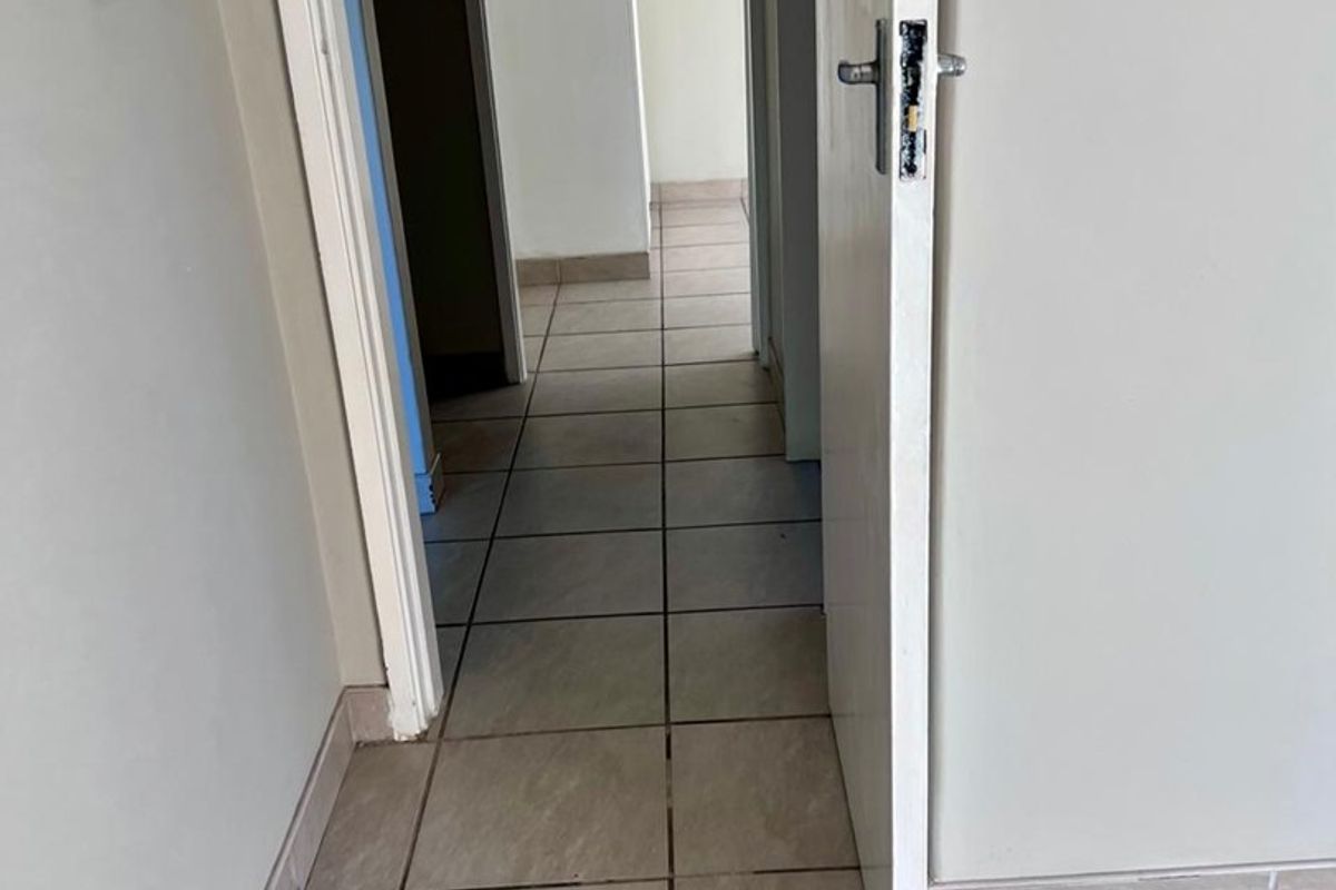 A vacant hallway featuring tiled flooring and neutral walls, providing access to adjacent rooms within the apartment.