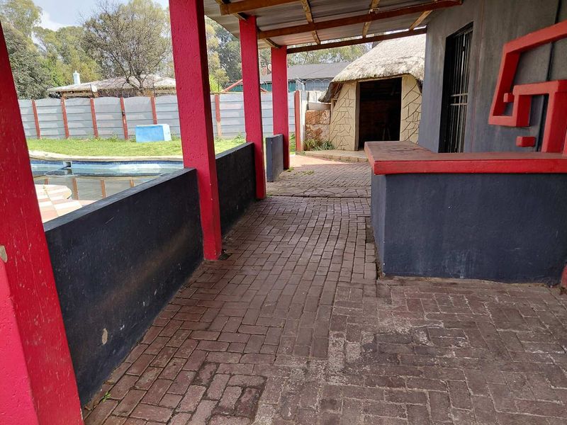 Covered outdoor patio area featuring a built-in bar counter, paved flooring, and direct access to the swimming pool and garden.