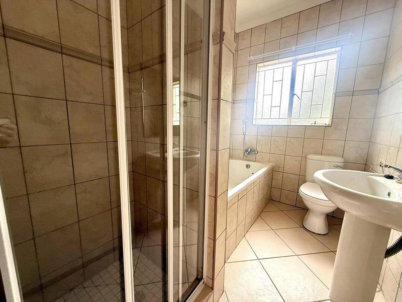 A functional bathroom featuring a shower enclosure, bathtub, pedestal basin, and toilet, finished with neutral wall and floor tiles.