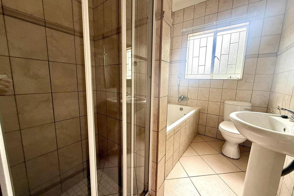 A functional bathroom featuring a shower enclosure, bathtub, pedestal basin, and toilet, finished with neutral wall and floor tiles.