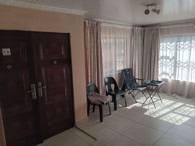 A living area featuring tiled flooring, security gates on windows, and a double entrance door, offering a functional space with potential for modernization.