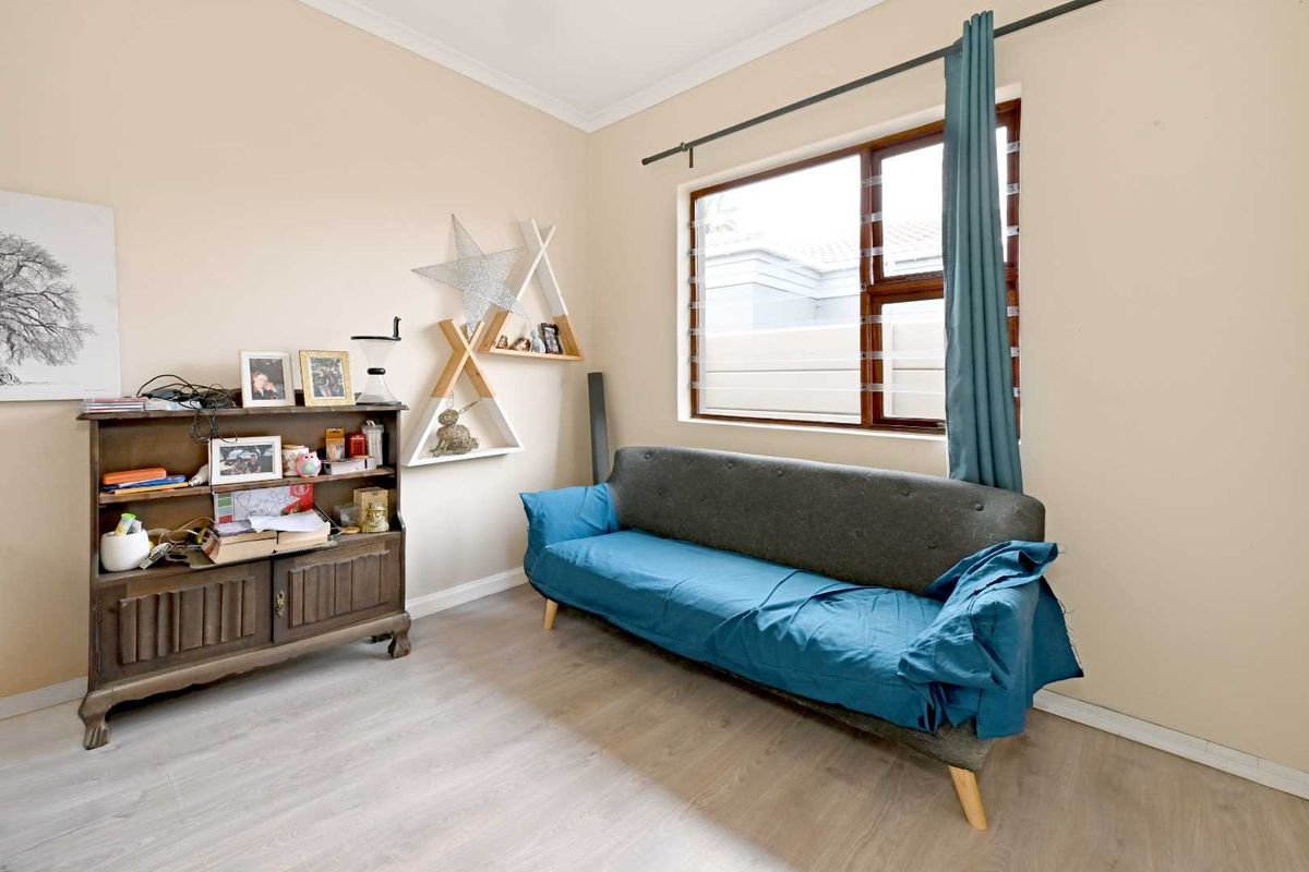 A living room featuring light-toned laminate flooring, a coved ceiling, and a large louvre-style window providing natural light.