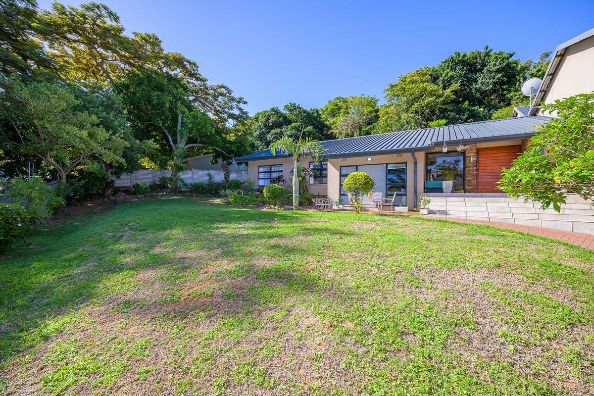 A spacious rear garden featuring a well-maintained lawn, mature trees, and a paved patio area adjacent to the house exterior.
