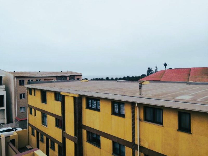 An elevated view of the apartment building exterior, showcasing the flat roof structure, plastered facade, and window placements.