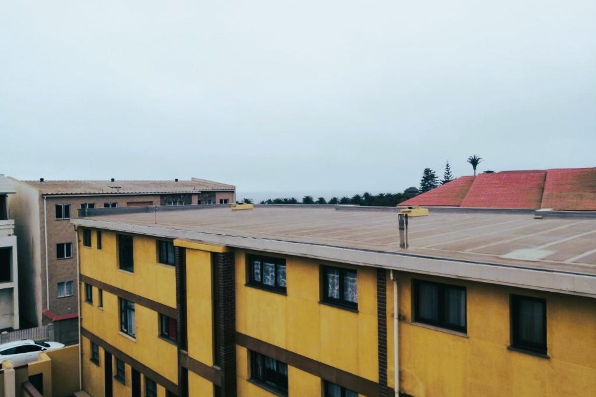 An elevated view of the apartment building exterior, showcasing the flat roof structure, plastered facade, and window placements.