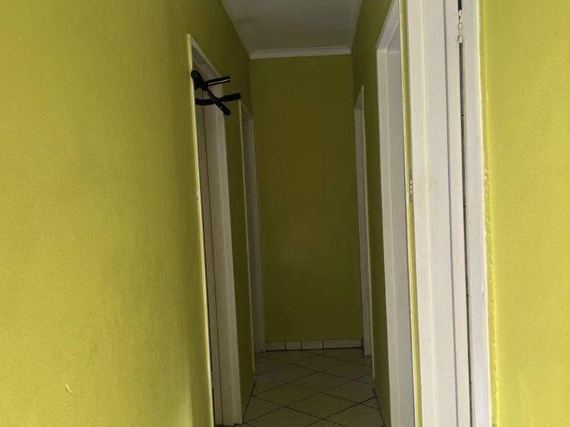 A narrow interior hallway featuring tiled flooring and multiple doorways, currently finished with bright green wall paint.