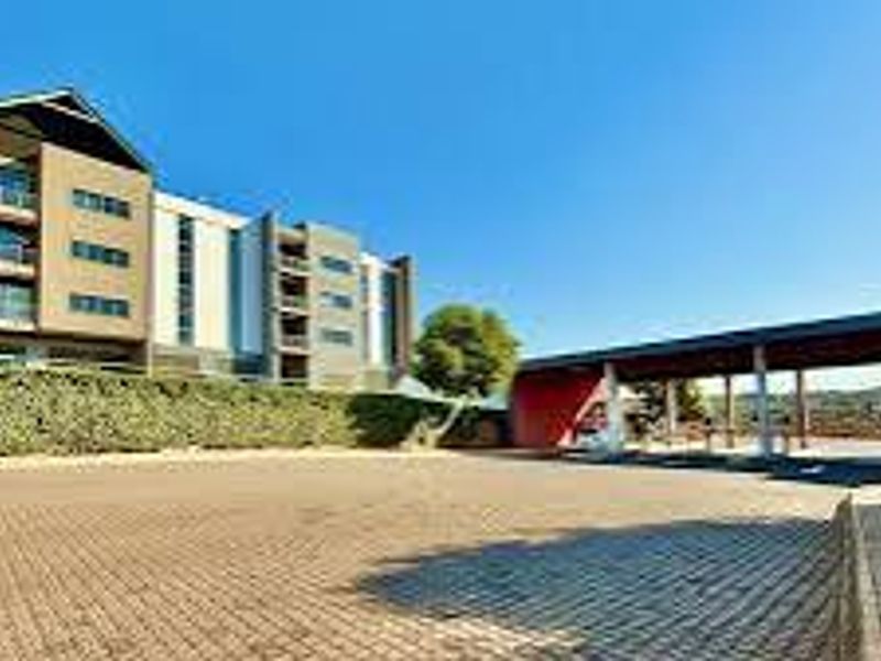 A view of the office building exterior featuring a paved driveway, retaining wall, and a covered entrance area.