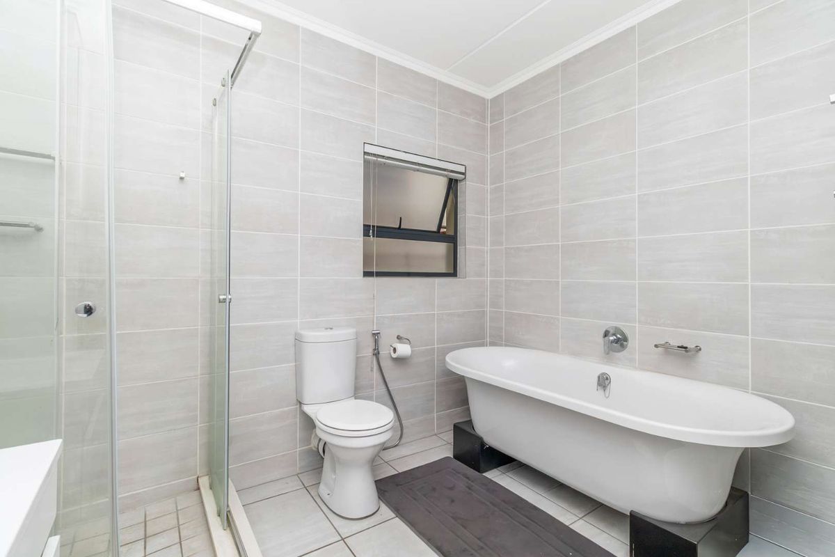 Modern bathroom featuring a freestanding bathtub, separate glass-enclosed shower, and neutral floor-to-ceiling ceramic tiling.