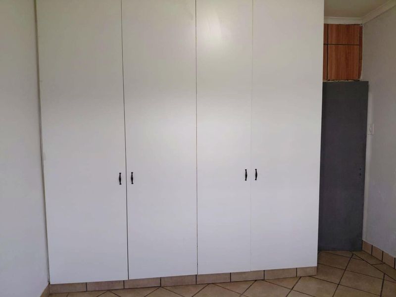 A bedroom featuring white built-in cupboards and tiled flooring, presenting a clean, neutral space ready for personalization.