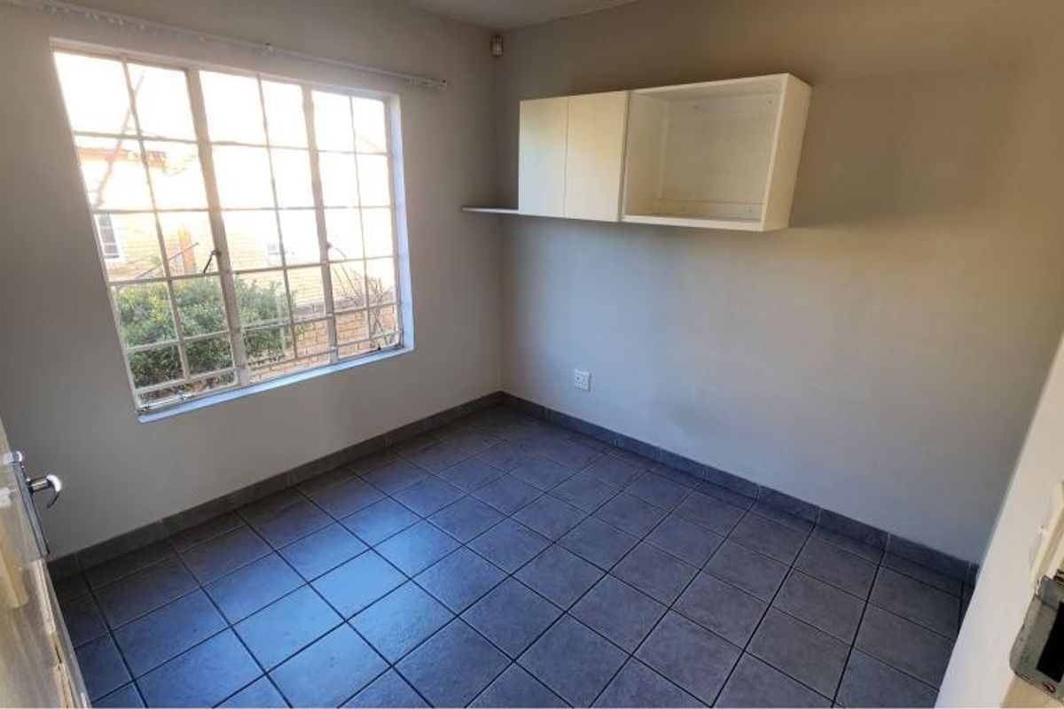 A vacant bedroom featuring tiled flooring, a steel-framed window, and built-in wall-mounted cabinetry, offering a blank canvas for personalization.