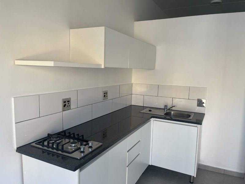 A clean, modern kitchen featuring white cabinetry, black granite countertops, a gas hob, and a subway tile backsplash.