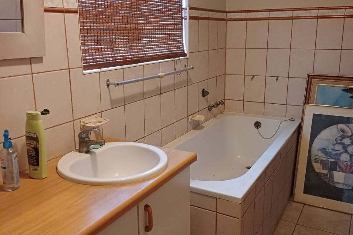 A functional bathroom featuring a built-in bathtub, tiled walls, and a vanity unit with a drop-in basin.