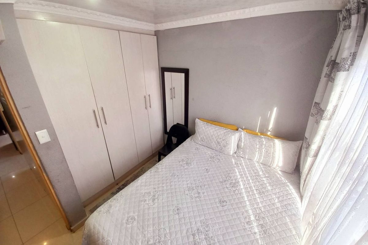 A compact bedroom featuring built-in white cabinetry, tiled flooring, and decorative ceiling cornicing.