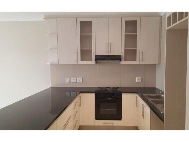 Modern kitchen featuring light wood-finish cabinetry, black granite countertops, integrated oven, hob, extractor fan, and a double bowl sink.