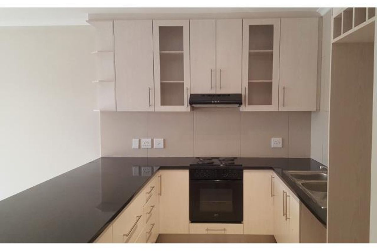 Modern kitchen featuring light wood-finish cabinetry, black granite countertops, integrated oven, hob, extractor fan, and a double bowl sink.