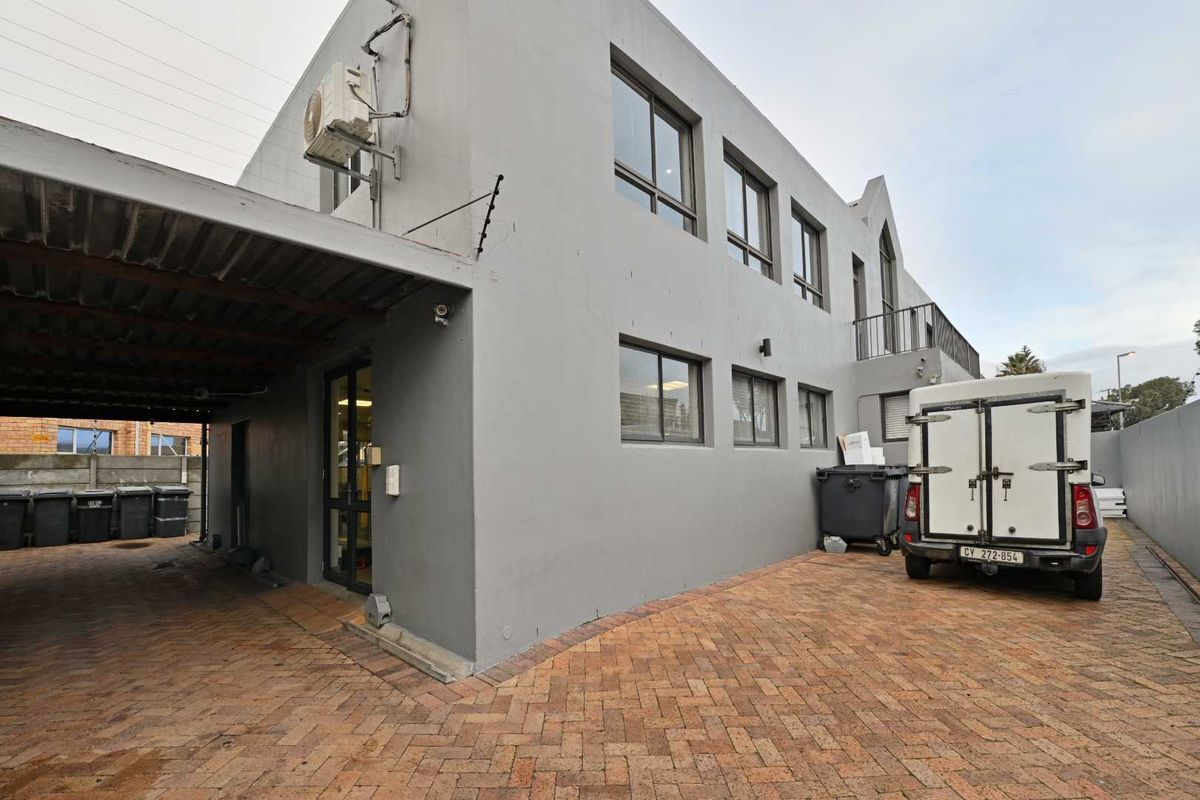 Rear exterior view of the mixed-use property featuring a paved driveway, covered parking area, and balcony access.