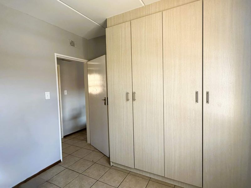 A clean, empty bedroom featuring light wood-finish built-in cupboards and neutral tiled flooring, offering a blank canvas for personalization.