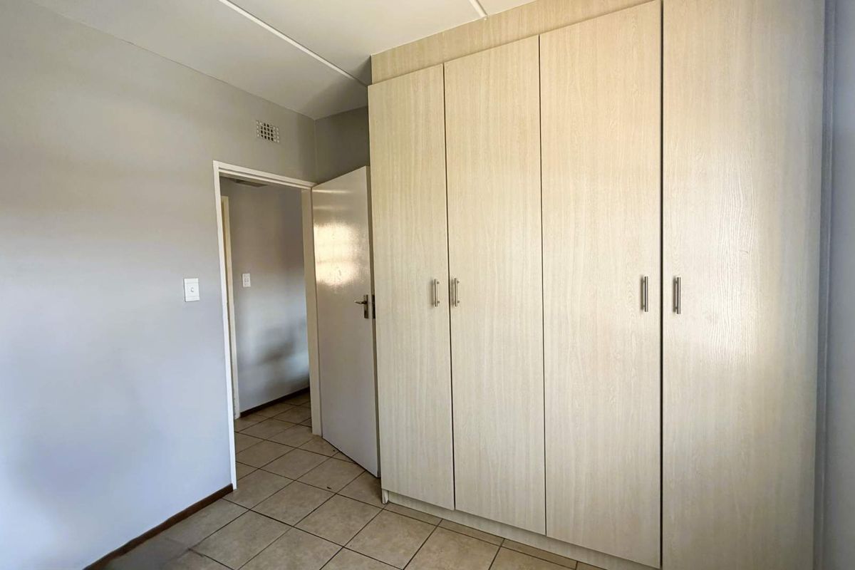 A clean, empty bedroom featuring light wood-finish built-in cupboards and neutral tiled flooring, offering a blank canvas for personalization.