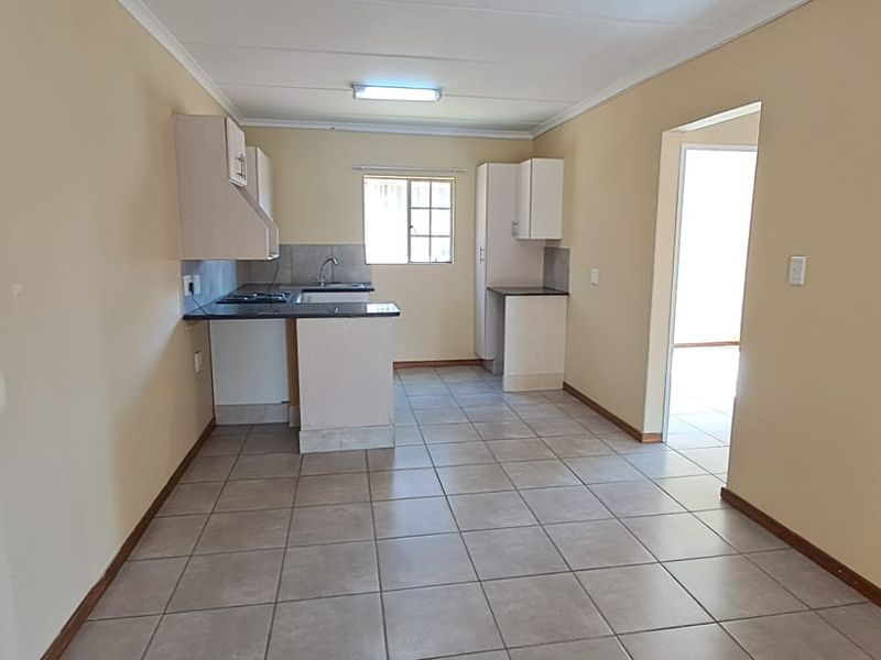 An open-plan kitchen and living area featuring tiled flooring, built-in cabinetry, and a functional layout, presenting a clean and neutral blank canvas.