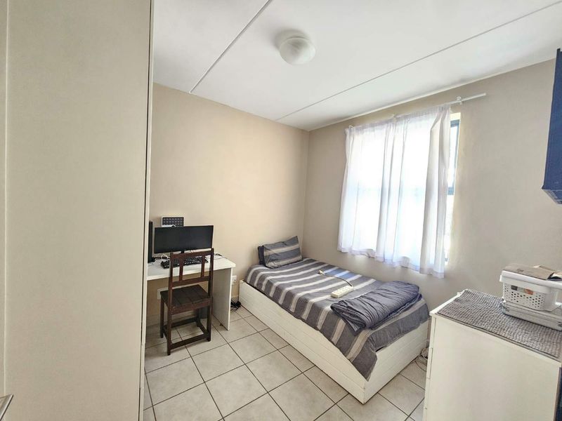A functional bedroom featuring tiled flooring, a built-in cupboard, and natural light through a window with curtains.