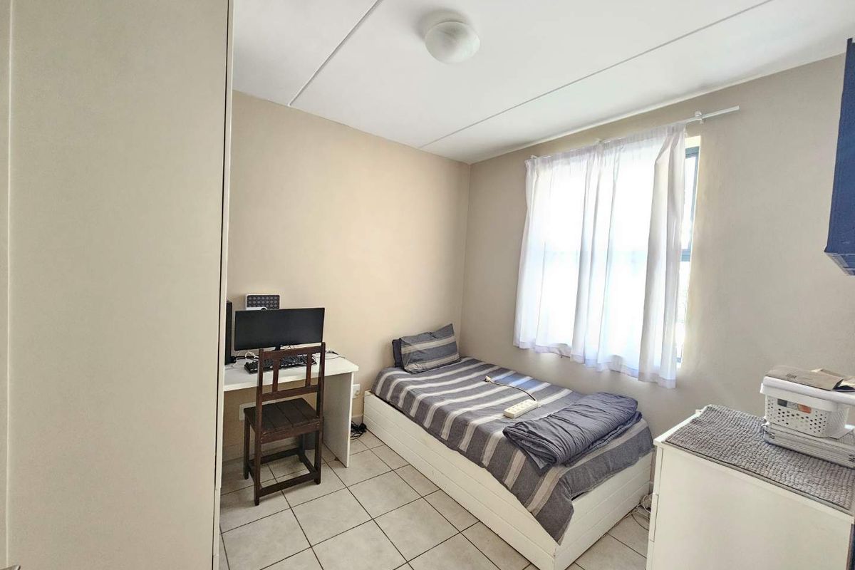 A functional bedroom featuring tiled flooring, a built-in cupboard, and natural light through a window with curtains.