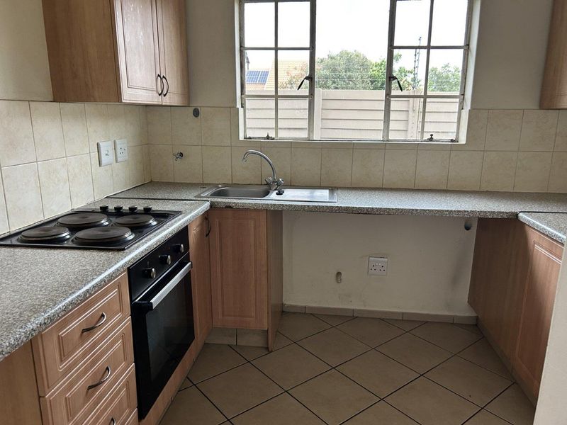 A functional kitchen featuring built-in cabinetry, laminate countertops, an electric hob, an oven, and a stainless steel sink with tiled finishes.