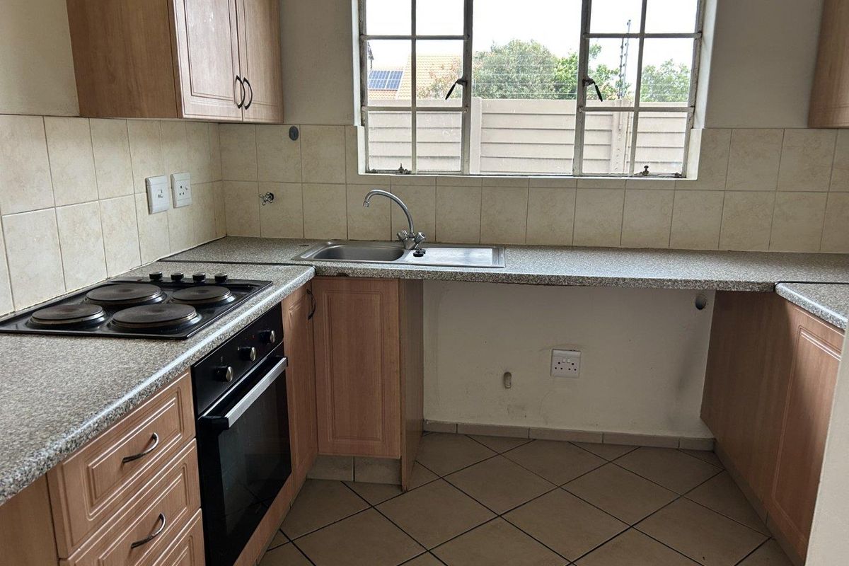 A functional kitchen featuring built-in cabinetry, laminate countertops, an electric hob, an oven, and a stainless steel sink with tiled finishes.