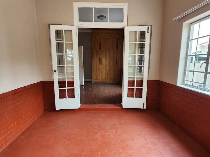 An empty living area featuring terracotta tile flooring, classic french doors with a transom window, and built-in wooden storage cupboards.