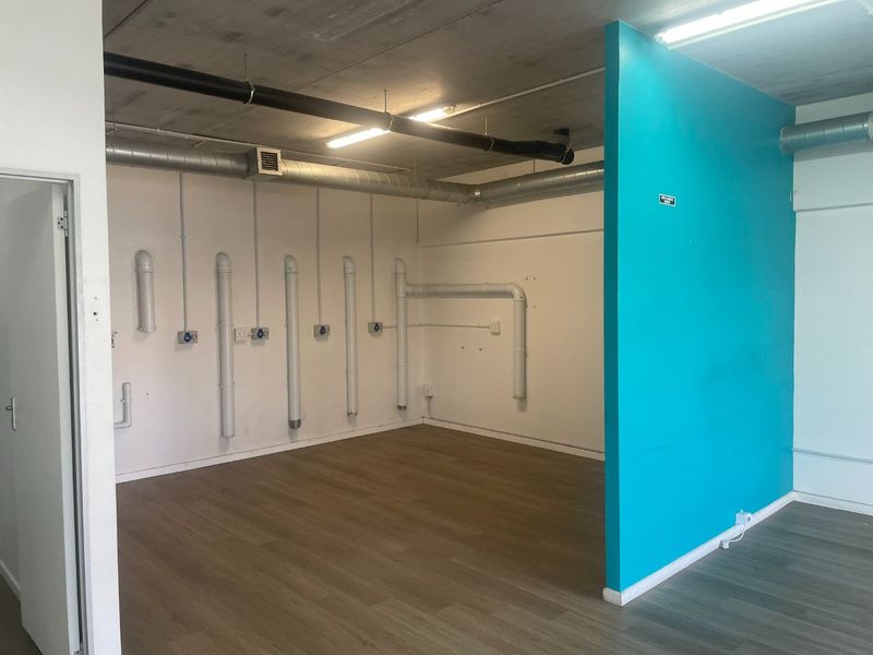 Open-plan utility space featuring exposed industrial-style ceiling, ducting, and plumbing, with laminate flooring and a vibrant blue partition wall.