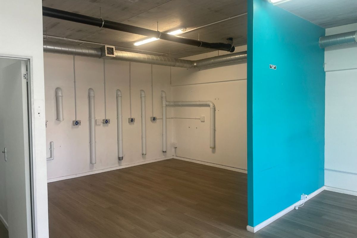 Open-plan utility space featuring exposed industrial-style ceiling, ducting, and plumbing, with laminate flooring and a vibrant blue partition wall.