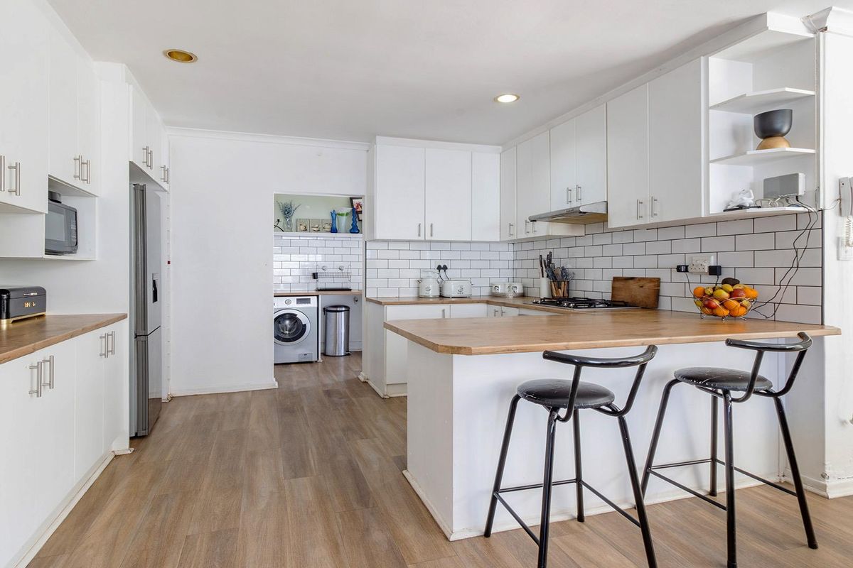 Modern kitchen featuring white cabinetry, timber countertops, subway tile backsplash, and a breakfast bar, with an adjacent laundry area visible.