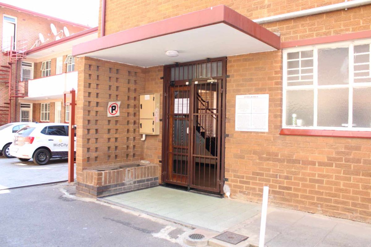 The apartment building entrance features a brick facade, a protective concrete canopy, and a secure metal gate leading into the complex.