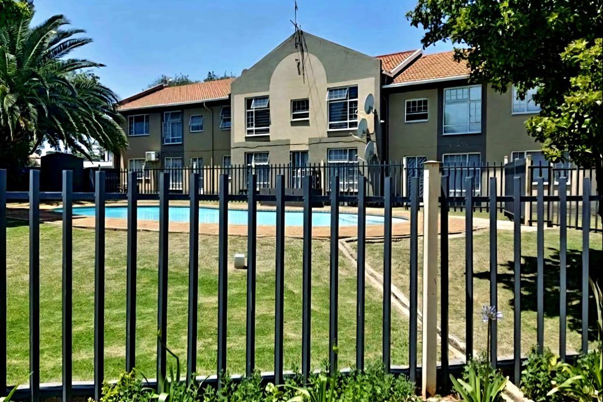 Exterior view of the townhouse complex featuring a communal swimming pool, manicured lawn, and secure perimeter fencing.
