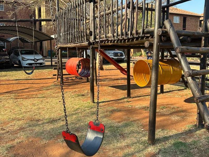 Outdoor communal playground area featuring a wooden climbing structure, swings, and tunnel slides located within the apartment complex grounds.