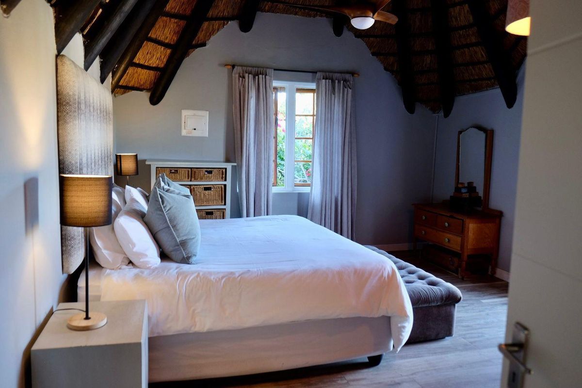 A cozy bedroom featuring a high vaulted thatched ceiling, exposed timber beams, and neutral wall finishes, creating a warm and inviting atmosphere.
