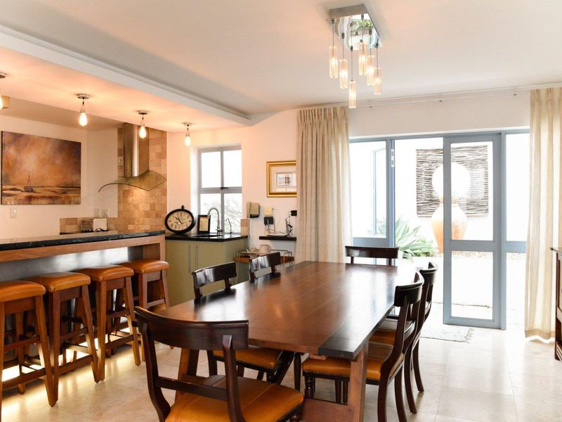 Spacious open-plan dining and kitchen area featuring a breakfast bar, stone countertops, modern lighting, and direct access to the patio through glass sliding doors.