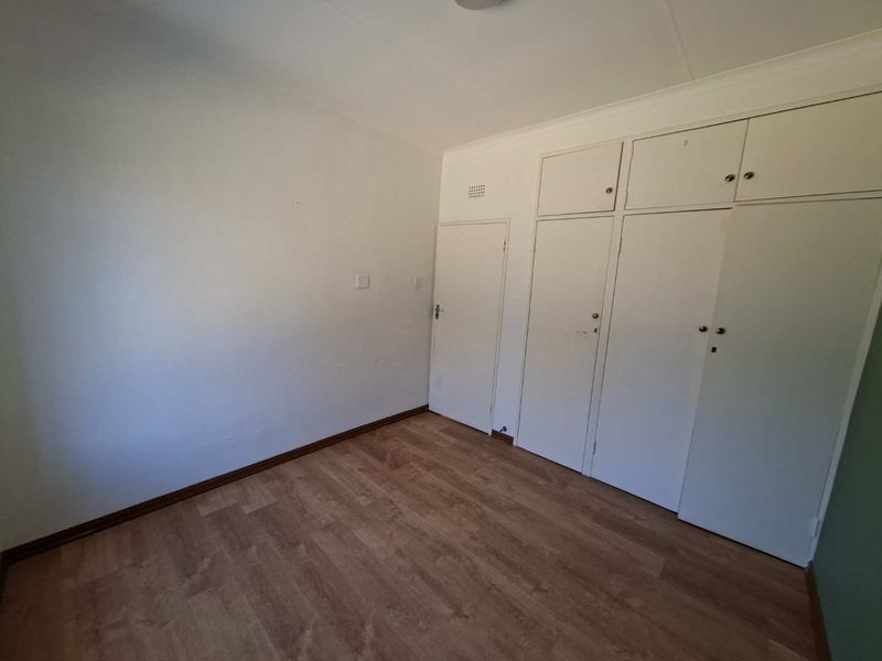 An empty bedroom featuring laminate flooring and extensive built-in cupboard storage with overhead cabinets.