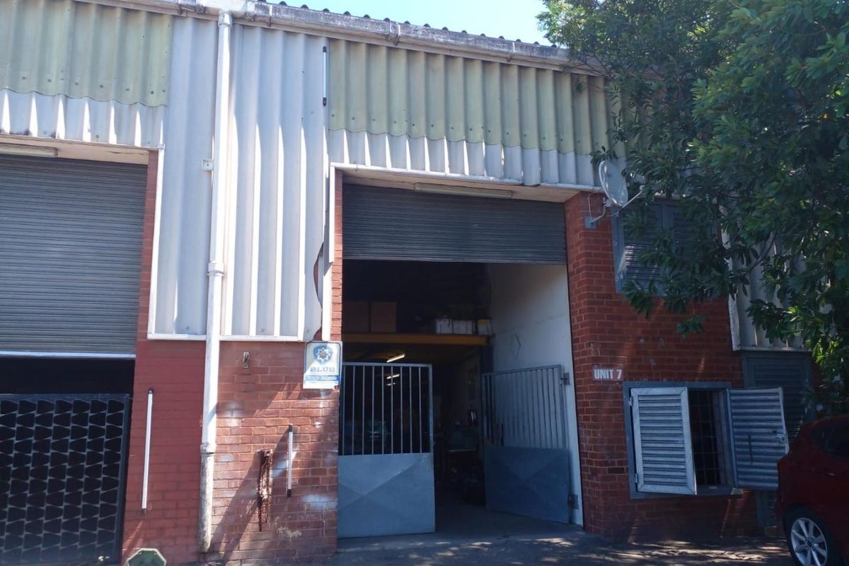 Front elevation of a retail unit featuring a roller shutter door, metal security gate, and a combination of brick and corrugated metal cladding.