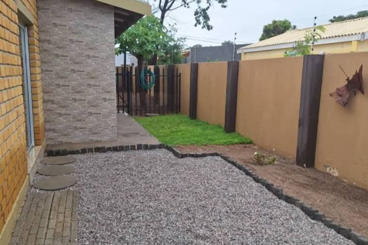 A well-maintained rear garden area featuring a gravel patio, paved walkway, and perimeter boundary wall with integrated security fencing.