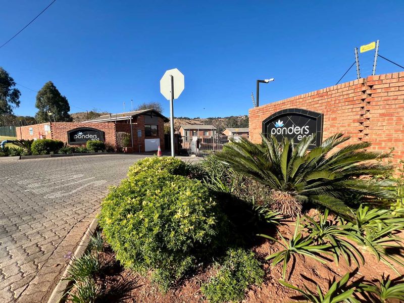 The entrance to Ponders End townhouse complex featuring a brick boundary wall, electric fencing, and a paved driveway leading to the security gate.