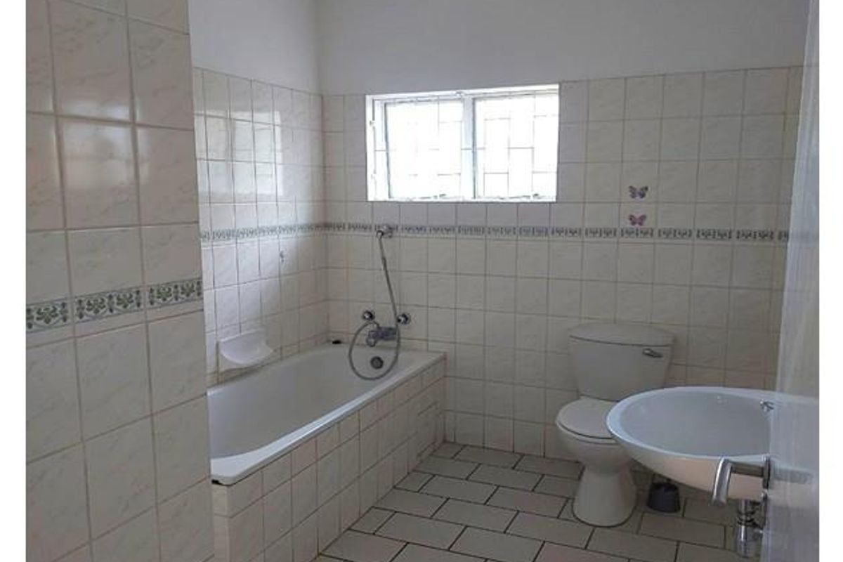 A functional bathroom featuring a built-in bathtub with shower mixer, a standard toilet, and a pedestal washbasin with tiled walls and flooring.