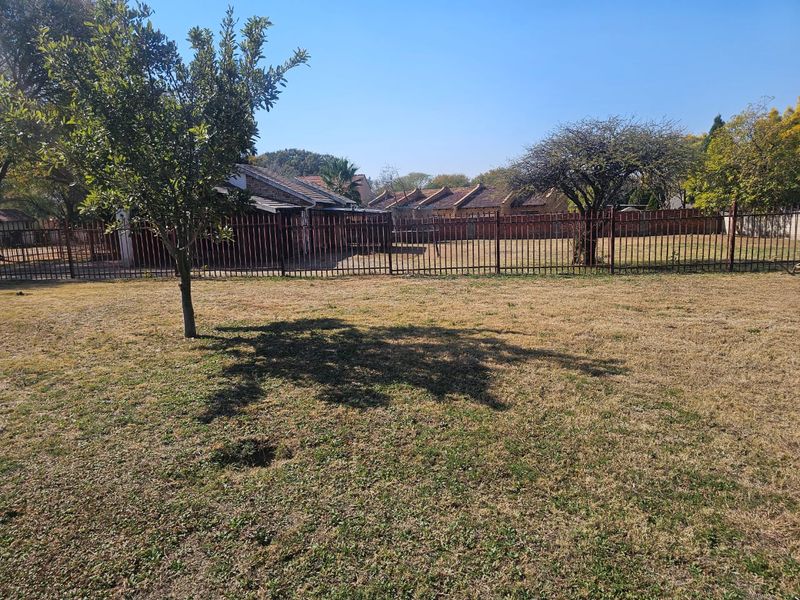 A spacious backyard area featuring a large lawn, mature trees, and secure metal perimeter fencing.