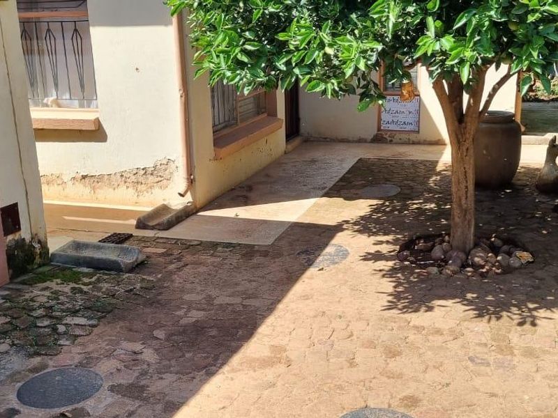 A rear courtyard area featuring paved surfaces, drainage infrastructure, and exterior wall access with visible plaster damage and signs of damp.