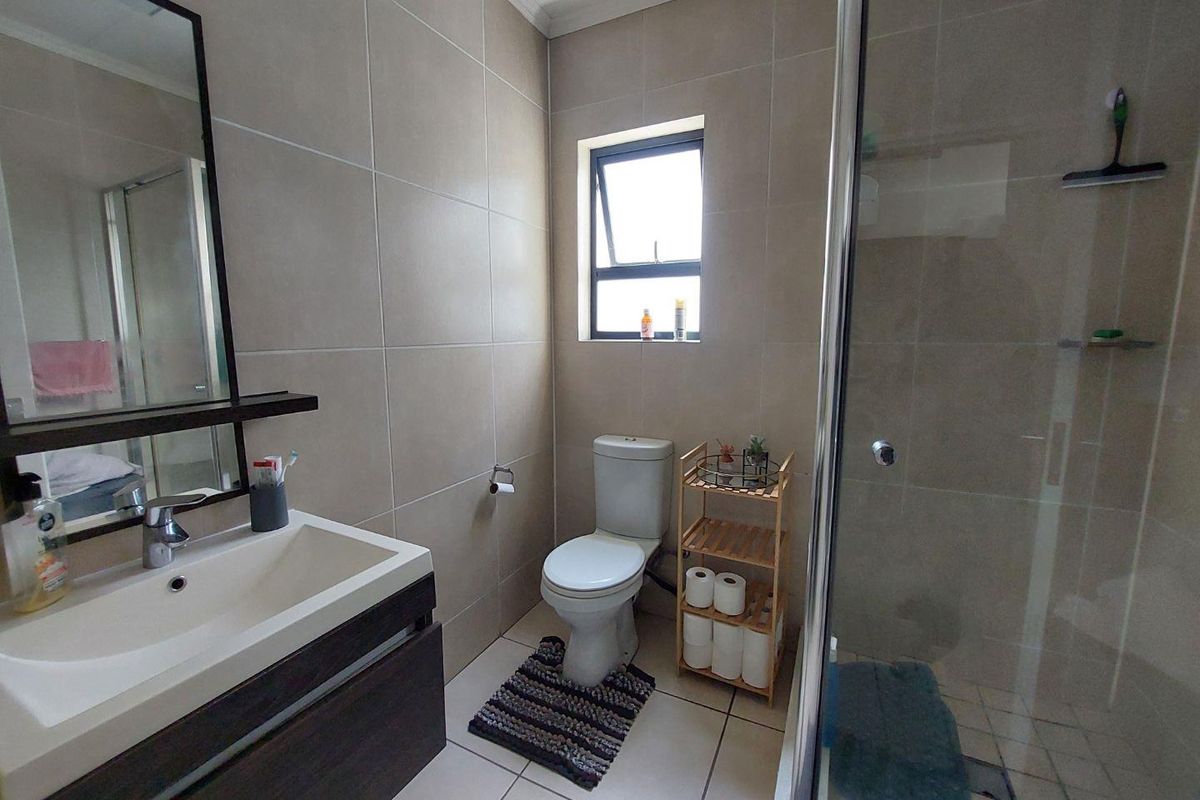 A modern bathroom featuring neutral wall tiles, a vanity with basin, a toilet, and a glass-enclosed shower.