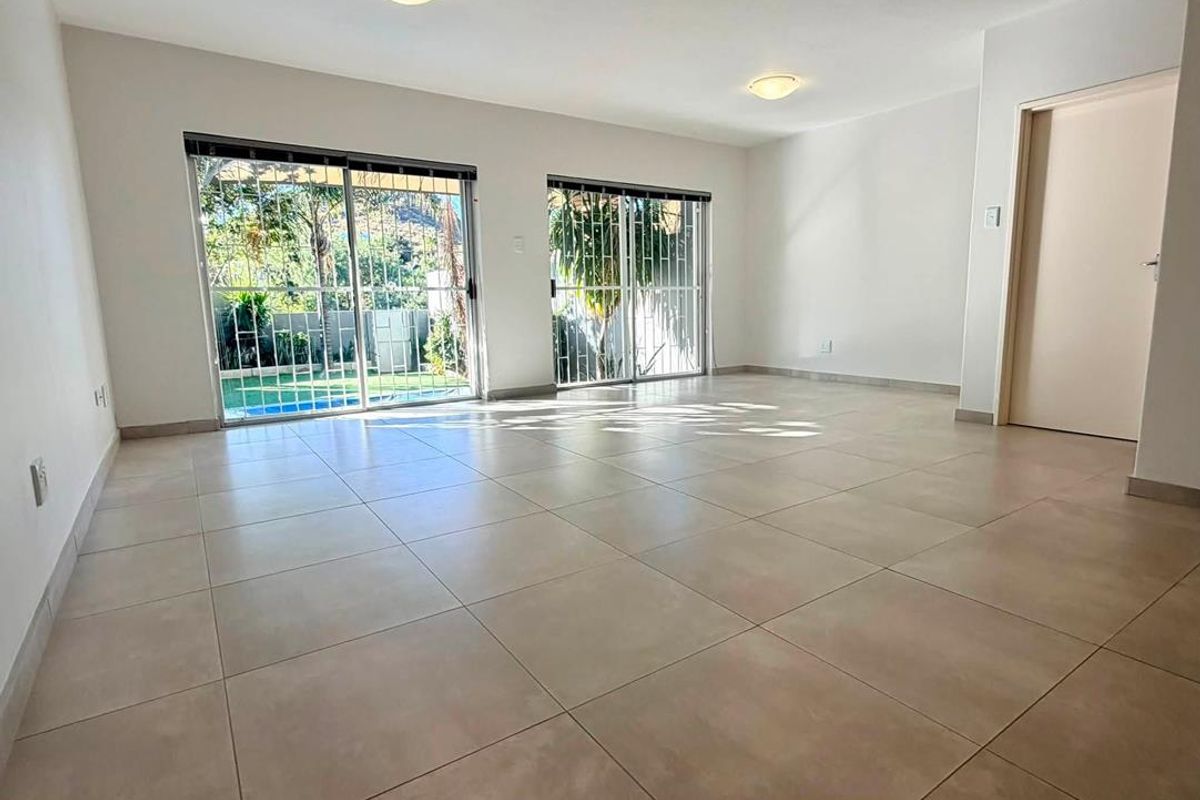 Spacious, light-filled living area featuring neutral floor tiles and dual sliding glass doors with security gates, providing direct access to the outdoor area.