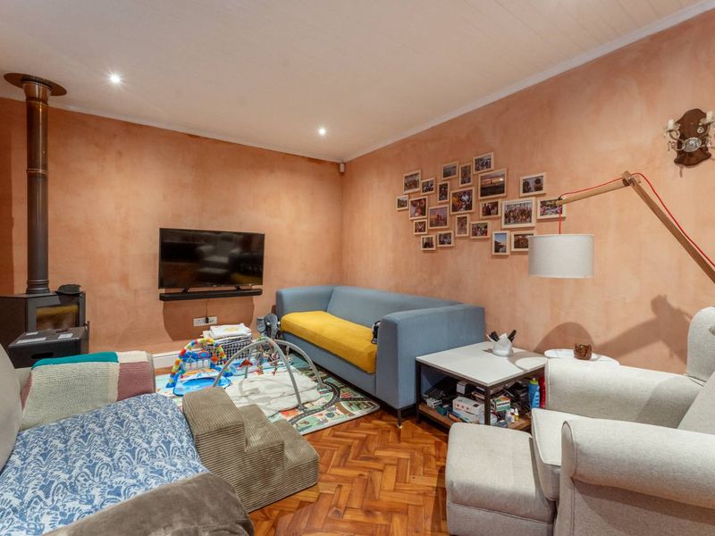 A cozy living room featuring warm-toned textured walls, classic parquet flooring, and a built-in wood-burning stove, creating a comfortable and inviting atmosphere.
