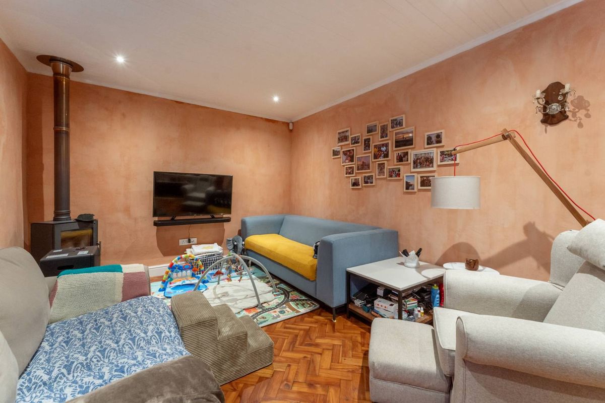 A cozy living room featuring warm-toned textured walls, classic parquet flooring, and a built-in wood-burning stove, creating a comfortable and inviting atmosphere.